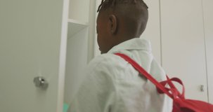 Video of african american boy closing locker and smiling at school. primary school education, knowledge and learning concept.