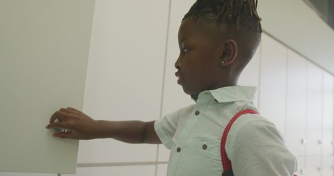 Video of african american boy closing locker and smiling at school. primary school education, knowledge and learning concept.