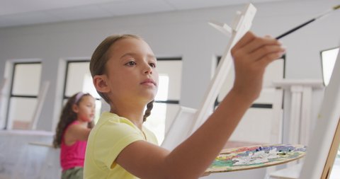 Video of focused caucasian girl painting during art lessons at school. primary school education, knowledge and learning concept.