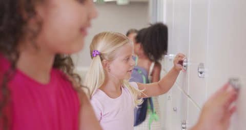 Video of happy diverse girls opening school lockers. primary school education, learning and socializing concept.