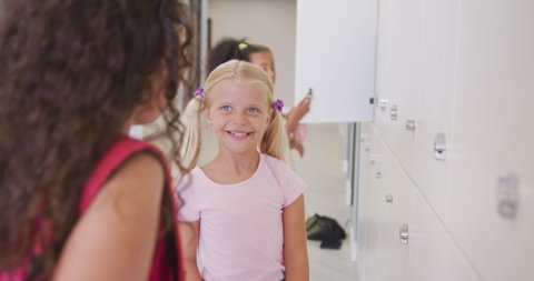 Video of happy diverse girls opening school lockers. primary school education, learning and socializing concept.