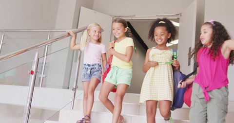 Video of happy diverse girls walking downstairs at school and talking. primary school education, learning and socializing concept.