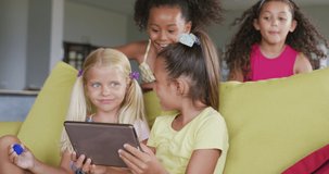 Video of diverse girls sitting at school common room with tablet, talking and laughing. primary school education, learning and socializing concept.