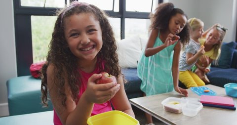 Video of happy biracial girl sitting with friends at school common room and eating. primary school education, learning and socializing concept.