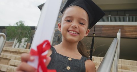 Video of happy caucasian girl wearing graduation hat and holding diploma. primary school education and graduation concept.