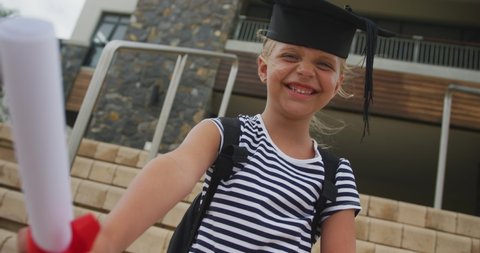 Video of happy caucasian girl wearing graduation hat and holding diploma. primary school education and graduation concept.