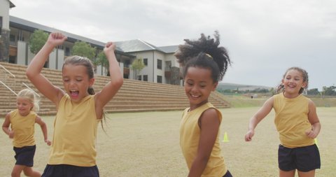 Video of happy diverse girls playing soccer in front of school. primary school education, sport and exercising concept.
