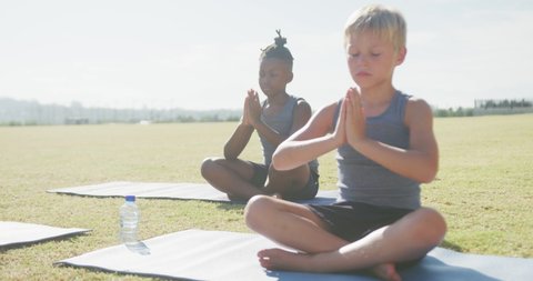 Video of focused diverse boys practicing yoga on mats on sunny day. primary school education, sport and exercising.