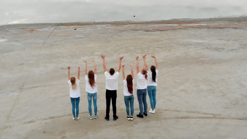 Young people stand in one line and wave their hands up. People greet the world by standing in an open space.