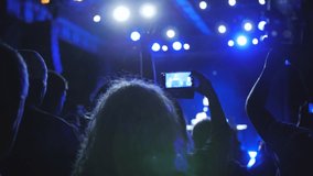 Unrecognizable Woman Hands Silhouette Recording Video of Live Music Concert with Smartphone. Shooting video on smartphone at rock concert. Crowd of people at music festival. Making video near stage.