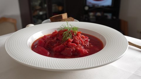 Traditional Ukrainian red soup or borscht  with red beetroot, potato, carrot, cabbage, beans on the white bowl, close up. Plate of red beetroot soup borsch rotates on table. Traditional Ukraine food