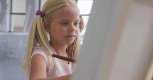 Video of focused caucasian girl painting during art lessons at school. primary school education, knowledge and learning concept.