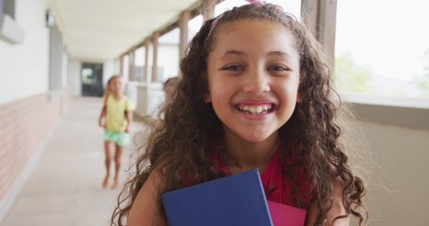 Video of happy biracial girl standing on school corridor. primary school education, learning and socializing concept.