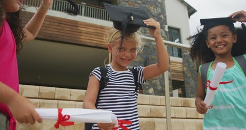 Video of happy diverse girls tossing hats after graduation. primary school education and graduation concept.