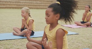 Video of focused diverse girls practicing yoga on mats in front of school. primary school education, sport and exercising concept.