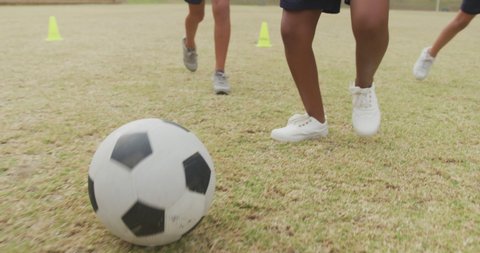 Video of legs of diverse girls playing soccer in front of school. primary school education, sport and exercising concept.