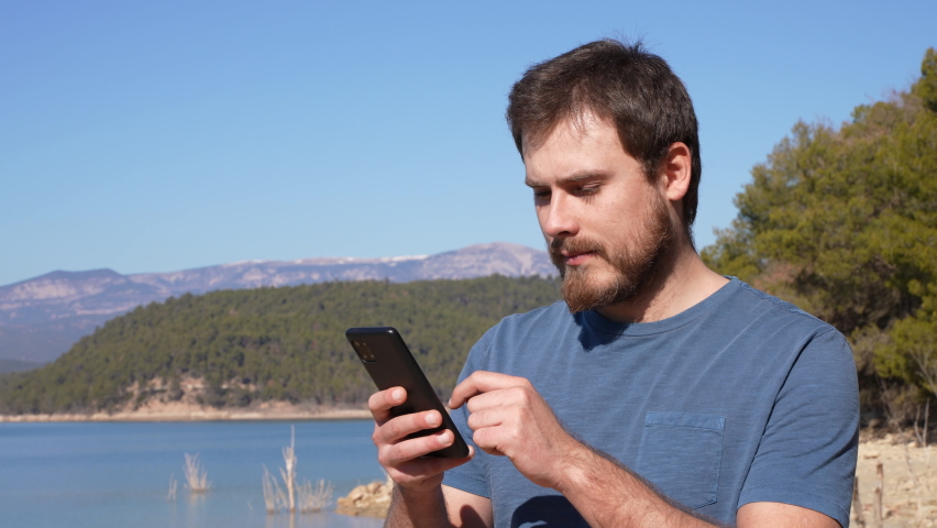 Surprised man checking phone finding good news outdoor in a lake