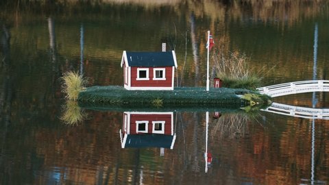 An idyllic scene in the town park in Sorreisa, Norway. Miniature houses with Norwegian flags in the middle of the lake reflected in the mirrorlike still water. Autumn foliage in the background.