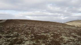 Cinematic aerial drone footage rising straight above heather and grouse moorland to reveal a mountain landscape with patches of snow and mountain bikers on a track. Morrane Ascent, Braemar, Scotland