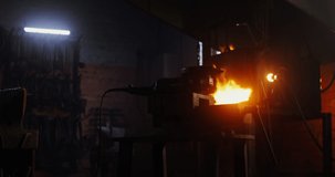 A blacksmith in protective gear and goggles takes an angle grinder and starts to cut off a part of a metal blank while working in a forge. 4k video, red komodo