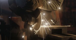 A blacksmith in protective equipment saws off a part of a metal stick using a flex, metal sparks fly in different directions, close-up, no face, unrecognizable person. 4k video, red komodo