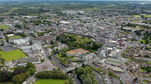 Aerial panoramic overall footage of town. Buildings and streets from height. Sport centre with play fields on waterfront. Ennis, Ireland