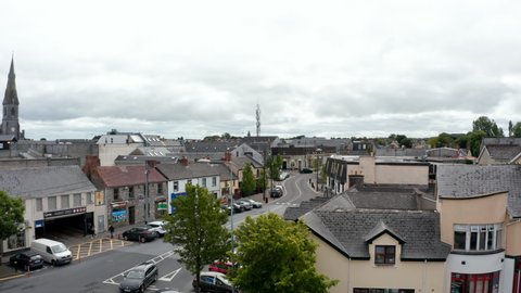 Forwards fly above buildings and street in town centre. Cars parked along road. Overcast sky. Ennis, Ireland