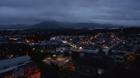 Aerial panoramic footage of evening town and mountains around lake in distance. Illuminated streets. Killarney, Ireland