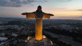 Drone flight around the statue of Jesus Christ in Lisbon. Jesus monument in sunset light. The god statue over the night landscape. Jesus protecting Portugal people.