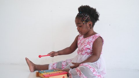 African American girl play with xylophone as toys and she look fun and happy in room with white background.