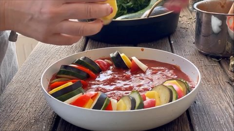 Women hands puts sliced vegetables in a bowl with tomato sauce. Ratatouille dish cooking preparation