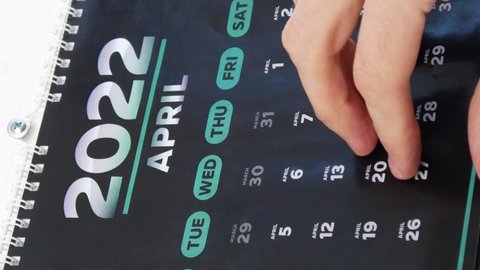 Close-up of male hands turning the wall calendar April page 2022 and pointing a finger at Eid al-Fitr date on the next one. Vertical video