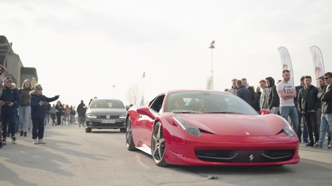 KRSKO, SLOVENIA – MARCH 2022: Street legal cars open meet. Red Ferrari expensive supercar arrive at cars exhibition surrounded by people 4K