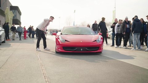 KRSKO, SLOVENIA – MARCH 2022: Street legal cars open meet. Red Ferrari expensive supercar arrive at cars exhibition with viewers looking 4K