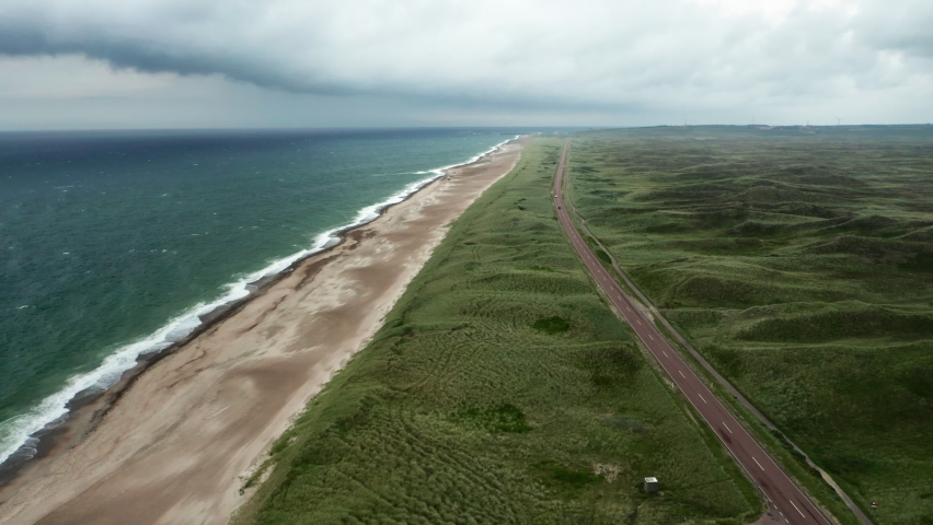 Wide Slow Motion Drone Flight Rising Over Grass Landscape And Road Next To Beach And Coastline Of Jutland, Westcoast Denmark Royalty-Free Stock Footage #1088602503