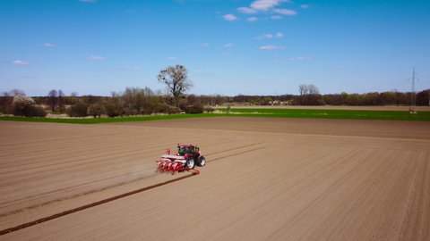 Aerial view of red tractor at work in spring field. Time of sowing. Shooting from drone flying over tractor in field with prepared soil for planting, new harvest. Agriculture concept. Rural landscape.