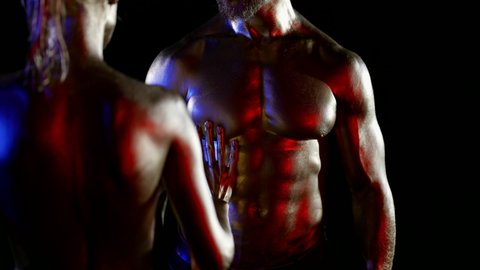 close-up of a couple with golden metallic skin on a black background. the woman is visible from the back and touches the male torso with hand. red, blue and white light. the dark key. without faces