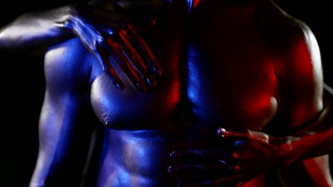 close-up of a muscular male torso with golden metallic skin. a woman stands behind a man and strokes chest with one hand, stomach with the other. red, blue and white light. without faces. dark key