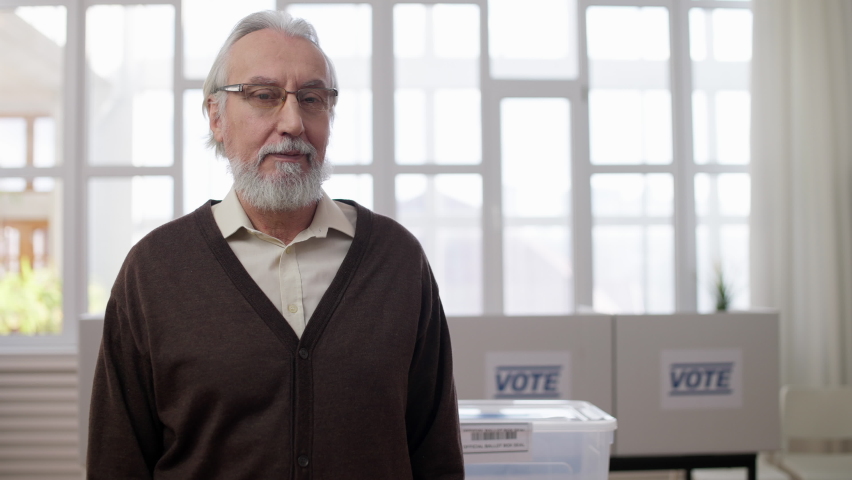 Senior man attaching vote pin on chest, smiling on camera, responsible citizen