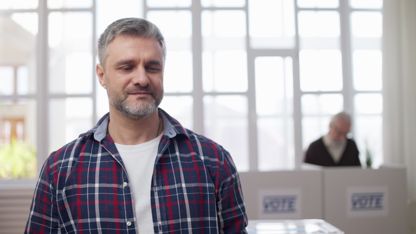 Smiling middle-aged man holding out vote button on camera, voting right and duty