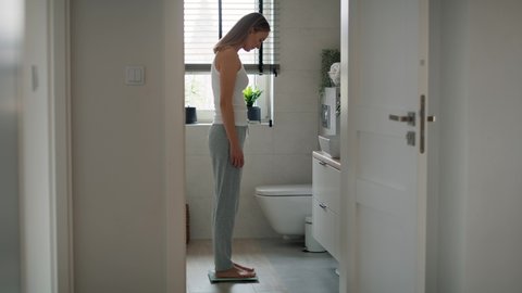 Frustrated caucasian woman stepping on bathroom scale. Shot with RED helium camera in 8K