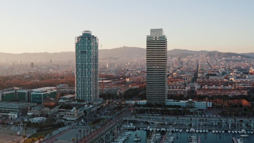 Aerial panorama of coastal district in modern Barcelona. Wide shot of skyscrapers twins Hotel Arts and Torre Mapfre, Peix Fish sculpture located before luxury harbor for sailing yachts in Port Olimpic