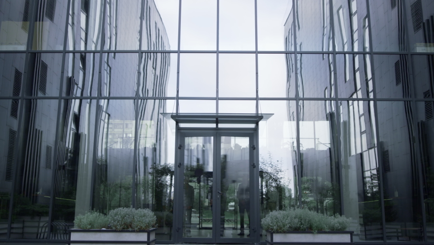 Successful businessman stand at office center door. Content team leave building. Handsome confident director leader posing at entrance. Satisfied team employees walking away. Business triumph concept.