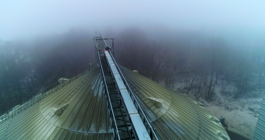 Big dirty rounded top of the granary tank. Flying along the metal support connecting the elevators. Top view on the winter foggy forest.