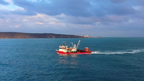 A red fishing boat underway towards Bosphorus Sea. Fisher boats sail at sunrise to catch school of fish. Offshore fishing contributes a significant income at Black Sea
