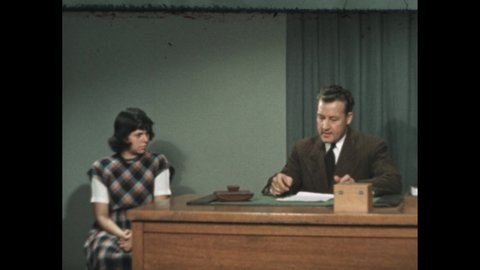 1940s: Man and girl in office sitting and talking. Girl shouts and yells. Man speaks back to her, and grabs a pen. Hand and pen correct grammar on handwritten note.