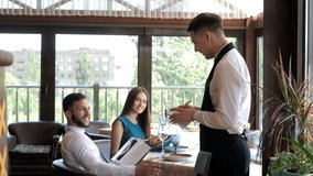 In A Restaurant, A Waiter Takes An Order From A Young Couple In An Elite Restaurant. Customer service. A waiter who gives recommendations in a restaurant.The customer reads the menu and makes an order - Powered by Shutterstock - Get 15% off with code: PIKWIZARD15