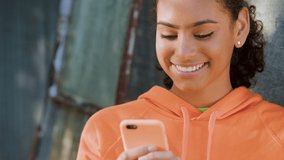 Beautiful, happy, smiling African AMerican biracial girl teenager young woman outdoors in the city using her smartphone or cell phone for social media or text messaging - Powered by Shutterstock - Get 15% off with code: PIKWIZARD15