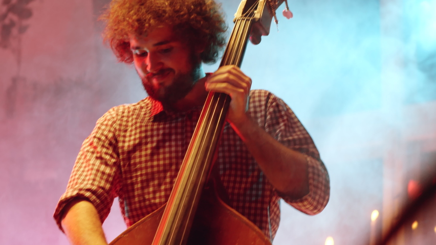 Handheld camera shot of young multiethnic band playing music and singing while performing live show on stage with smoke and neon light