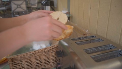 Woman puts bagel in toaster for breakfast